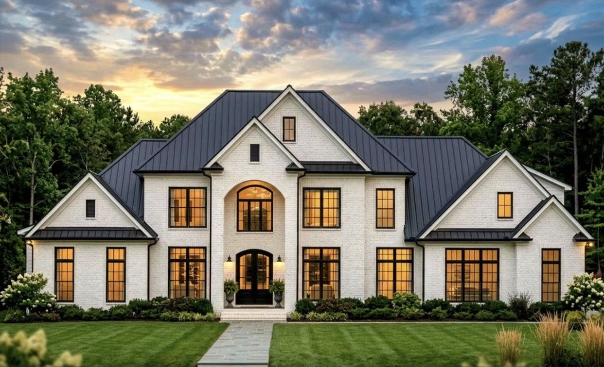 White brick home with a black metal roof and arched entry at dusk